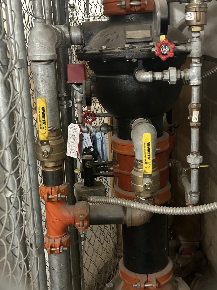 Fire sprinkler riser with control valve, gauges, and inspection tags at a Texas commercial site